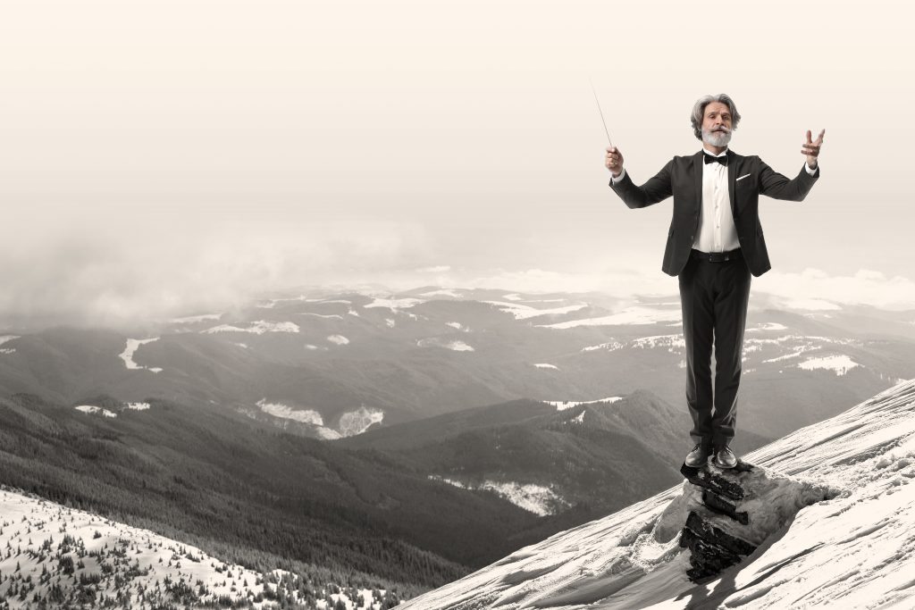 Silhouette of alone tourist standing on snowy mountain top in winner pose with raised hands enjoying view and achievement on bright sunny winter day. Adventure, outdoors activities, healthy lifestyle.